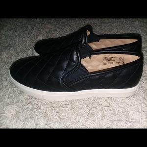 Black slid on shoes with checked embroidered design.